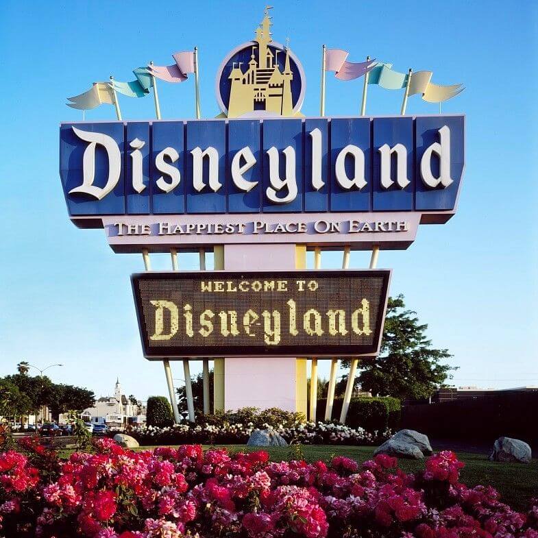 disneyland sign, over the top usage of flags, bright lights, saying "Welcome to Disneyland, The Happiest Place On Earth"